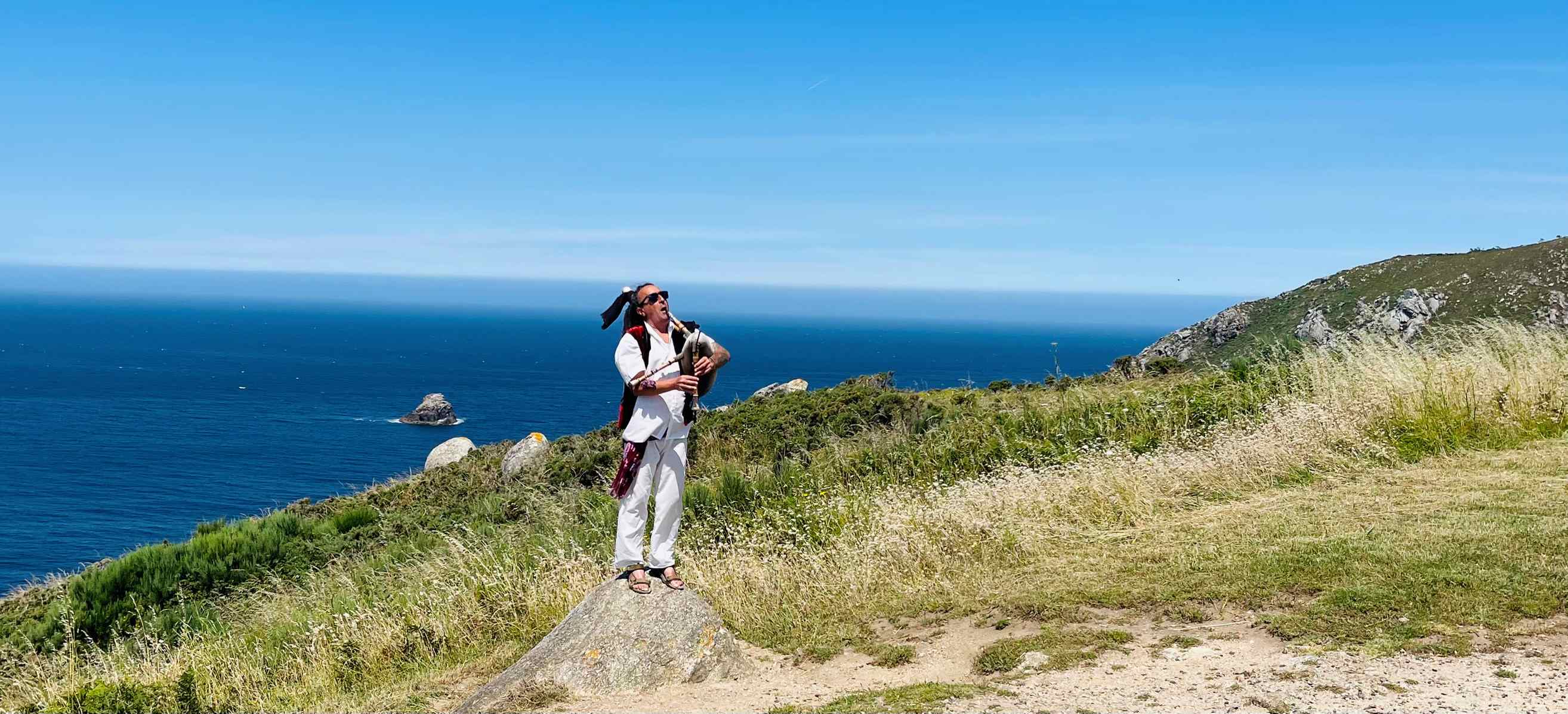 Bagpiper on a hill with bright blue ocean behind him in Finisterre, Spain
